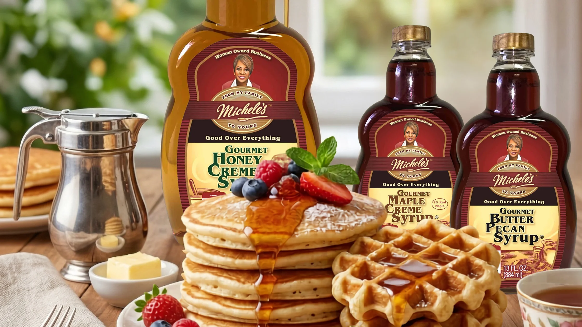 Tall stack of fluffy pancakes topped with raspberries, blueberries, and syrup, with Michele’s buttermilk pancake and waffle mix in the background.